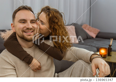 Woman whispering to smiling man while relaxing together on sofa at home 136965347