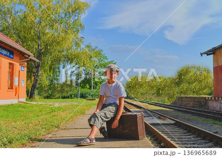 Little boy on a railway station, waiting for the train with vintage suitcase. Traveling, holiday and chilhood concept. Travel insurance concept. Travel, tourism, summer vacation and family concept Little boy on a railway station, waiting for the train with vintage suitcase. Traveling, holiday and chilhood concept. Travel insurance concept. Travel, tourism, summer vacation and family concept 136965689
