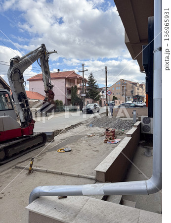 Excavator working on residential street construction site. Urban infrastructure, civil engineering, road repair, suburban development 136965931