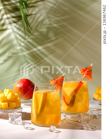 Homemade cocktail, juice, or lemonade with mango slices and ice on a sun-drenched kitchen table. Summer party concept. Refreshing summer diet drink recipe, detox diet and healthy lifestyle Homemade cocktail, juice, or lemonade with mango slices and ice on a sun-drenched kitchen table. Summer party concept. Refreshing summer diet drink recipe, detox diet and healthy lifestyle 136967462