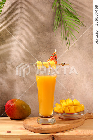 Homemade cocktail, juice, or lemonade with mango slices and ice on a sun-drenched kitchen table. Summer party concept. Refreshing summer diet drink recipe, detox diet and healthy lifestyle, 136967469