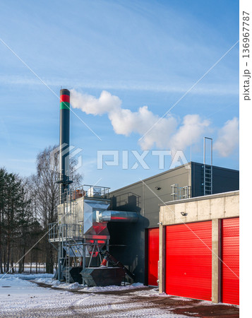 Modern wood chip biomass boiler house with smokestack operating in winter under clear blue sky Modern wood chip biomass boiler house with smokestack operating in winter under clear blue sky 136967787