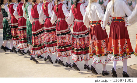 Women in traditional embroidered folk dresses dancing in synchronized movement at cultural festival. Bulgaria heritage, national identity, folk horo dance tradition, artistic craftsmanship of region 136971303