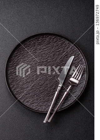 An empty round ceramic plate, knife, and fork as a dining table setting. An empty plate 136972749