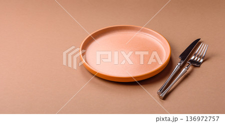 An empty round ceramic plate, knife, and fork as a dining table setting. An empty plate An empty round ceramic plate, knife, and fork as a dining table setting. An empty plate 136972757