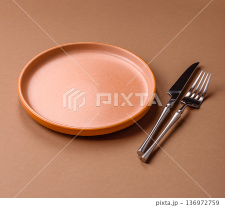 An empty round ceramic plate, knife, and fork as a dining table setting. An empty plate An empty round ceramic plate, knife, and fork as a dining table setting. An empty plate 136972759