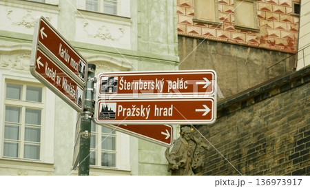 Pedestrian directional signpost information Prague Castle and Sternberg Palace in Nerudova Charles Bridge major tourist attractions usable helpful street sign walking city guide white text brown color 136973917
