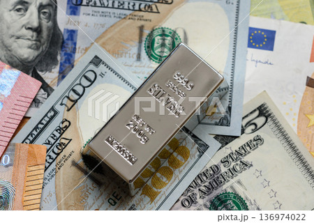 A silver bar, white metal against a backdrop of money, as a concept for the sales. A silver bar 136974022