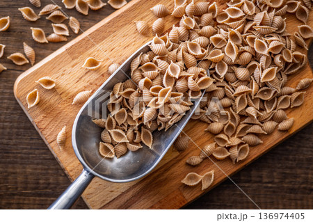 Wholegrain conchiglie pasta on scoop on wooden table. Top view. Wholegrain conchiglie pasta on scoop on wooden table. Top view. 136974405