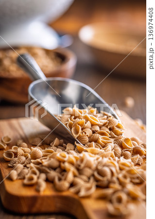 Wholegrain conchiglie pasta on scoop on wooden table. Wholegrain conchiglie pasta on scoop on wooden table. 136974408