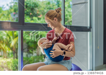 Young mother gently rocks her baby on a fitness ball at home, creating a calm loving atmosphere. Authentic family lifestyle, natural parenting and emotional bonding. Motherhood, wellbeing and baby Young mother gently rocks her baby on a fitness ball at home, creating a calm loving atmosphere. Authentic family lifestyle, natural parenting and emotional bonding. Motherhood, wellbeing and baby 136974416