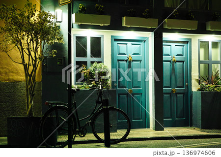 Traditional building facade featuring teal colored wooden doors decorated with cicada shaped door knockers and a black bicycle parked nearby Traditional building facade featuring teal colored wooden doors decorated with cicada shaped door knockers and a black bicycle parked nearby 136974606