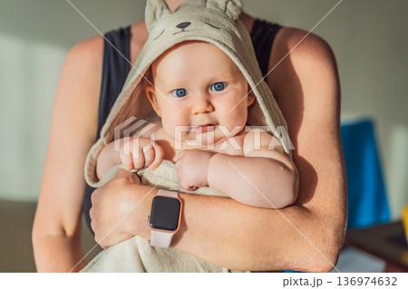 Mother holding her baby wrapped in a soft towel after bath at home, sharing a warm caring moment. Authentic parenthood scene showing love, safety and comfort. Baby hygiene, wellbeing and family 136974632