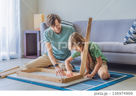 Father and his son assembling a table together in the living room at home. Meaningful family moment showing teamwork, learning and support. Fatherhood, home improvement and bonding through shared Father and his son assembling a table together in the living room at home. Meaningful family moment showing teamwork, learning and support. Fatherhood, home improvement and bonding through shared 136974909