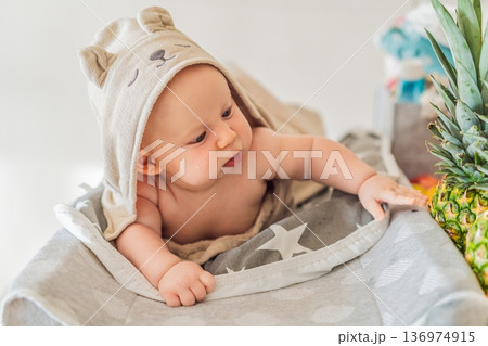 Baby lying on a changing table wrapped in a soft towel after bathing at home. Clean, calm and cozy moment of infant care and safety. Baby hygiene, daily routine and gentle parenting concept 136974915