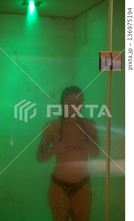 Peaceful woman standing amid soft emerald glow with dewy skin 136975194
