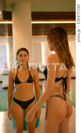 Pair of women in swimsuits chat near sparkling pool with warm glow 136975199