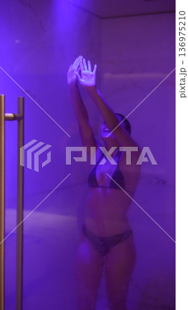 Elegant bikini model performing dance within misty shower setting Elegant bikini model performing dance within misty shower setting 136975210