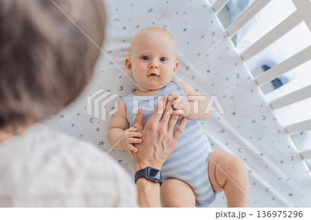 Father gently placing his baby into a crib at home, creating a calm and safe bedtime moment. Caring fatherhood scene filled with trust and warmth. Parenting, infant sleep and family bonding concept 136975296