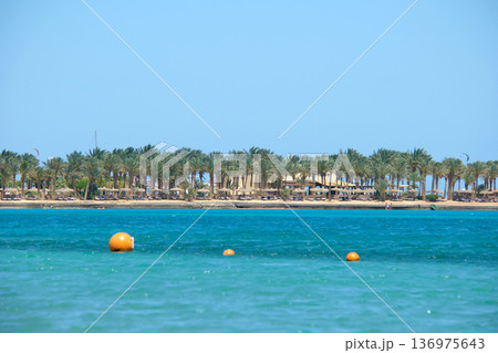Yellow buoys floating on sea surface as marker for swimming restriction in deep water at tropical resort with view of coast line in distance. Human life safety concept. Yellow buoys floating on sea surface as marker for swimming restriction in deep water at tropical resort with view of coast line in distance. Human life safety concept. 136975643