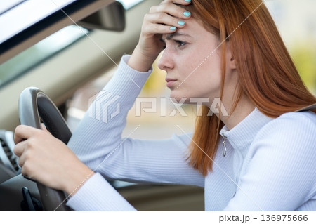 Sad tired yound woman driver sitting behind the car steering wheel in traffic jam. Sad tired yound woman driver sitting behind the car steering wheel in traffic jam. 136975666