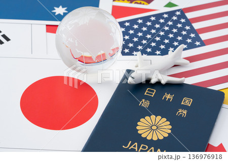 たくさんの国旗のカードを背景に青色の日本のパスポートと飛行機と地球のミニチュア 136976918