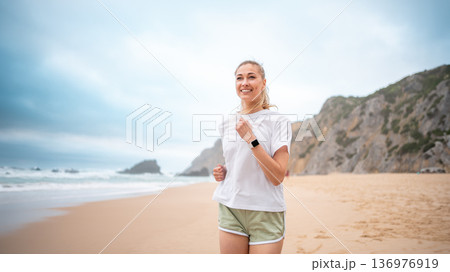 Smiling fit woman jogging along sandy beach in 136976919