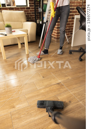 Couple cleaning hardwood floors, using vacuum and mop to keep home neat and organized on sunny afternoon. Individuals maintaining tidy living room and completing daily household chores. Couple cleaning hardwood floors, using vacuum and mop to keep home neat and organized on sunny afternoon. Individuals maintaining tidy living room and completing daily household chores. 136977274