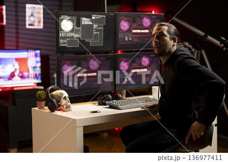 Hacker in hideout preparing to escape before getting caught after being found by police while writing malware code on computer. Man in criminal den found by anti hacking law enforcement 136977411