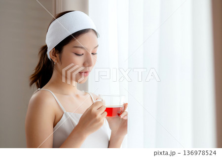 Beautiful young asian woman with headband enjoying tea standing near window with satisfied. Beautiful young asian woman with headband enjoying tea standing near window with satisfied. 136978524
