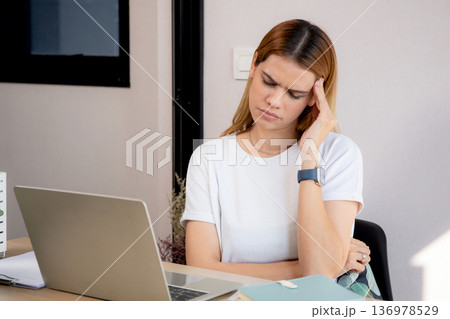 Unhappy young caucasian businesswoman using laptop computer on desk with stress and burnout. Unhappy young caucasian businesswoman using laptop computer on desk with stress and burnout. 136978529