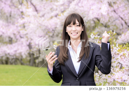 桜の前でガッツポーズをするスーツを着た女性 桜の前でガッツポーズをするスーツを着た女性 136979256