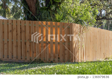 Wooden picket fence on green lawn surrounding property grounds for backyard protection and privacy Wooden picket fence on green lawn surrounding property grounds for backyard protection and privacy 136979636