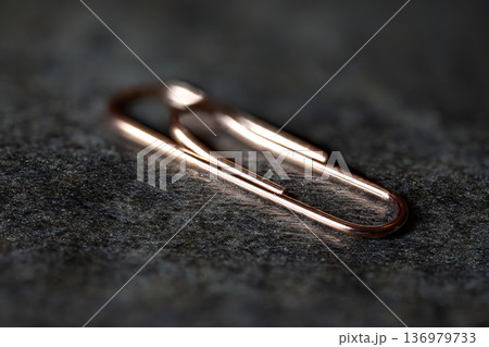 Selective focus macro shot of a single copper-colored paperclip on a dark textured background Selective focus macro shot of a single copper-colored paperclip on a dark textured background 136979733