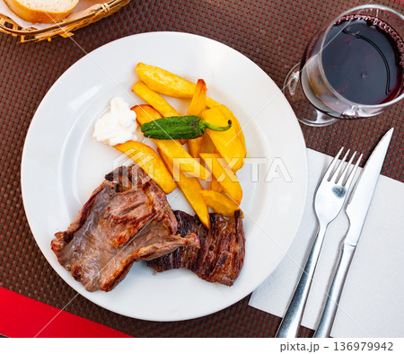 on large white plate heaps of fried beef seasoned with green pepper with fried potatoes and sauce 136979942