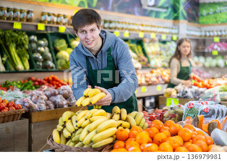 Young salesman placing bananas in a market basket in large grocery store Young salesman placing bananas in a market basket in large grocery store 136979981