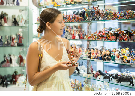 Female buyer holds in hands tests figurine she-dancer flamenco in memorable gifts shop 136980005