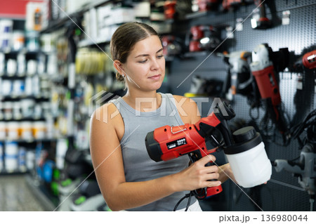 Woman choose examines spray gun airbrush in tools department of construction store Woman choose examines spray gun airbrush in tools department of construction store 136980044