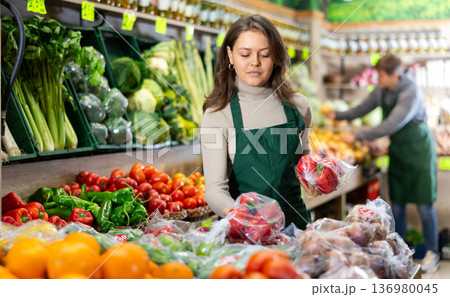 Saleswoman fills grocery store window with ripe bell peppers 136980045
