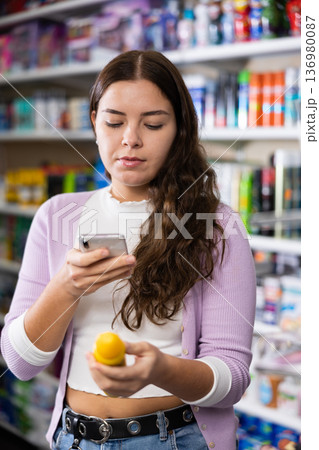 Portrait of smiling woman consumer choosing product at beauty shop, using smartphone for scanning barcode 136980087