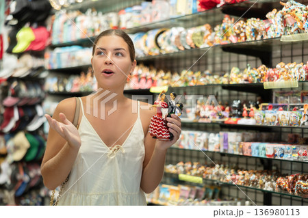 Happy young woman choosing statue of Spanish dancer among various souvenirs in gift shop in Barcelona 136980113
