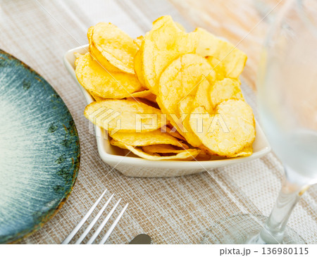 Close-Up Of tasty potato chips or crisps in white square plate on table 136980115