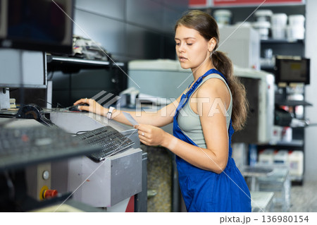 Young woman worker operating computerised machine to mix paint in paint shop 136980154