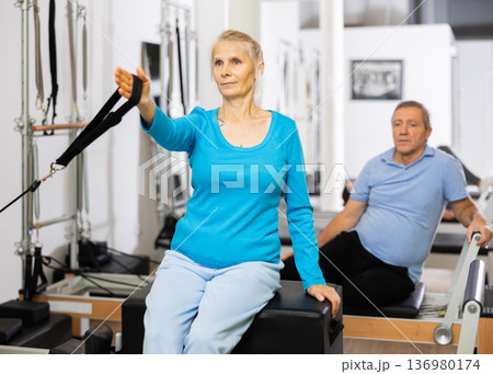 Elderly woman performing toning Pilates exercise for arms during group class in rehabilitation center 136980174