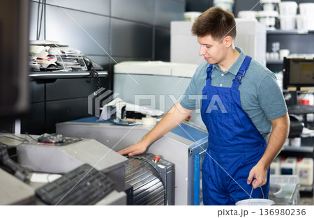Man in uniform operating computerised machne to mix paint 136980236