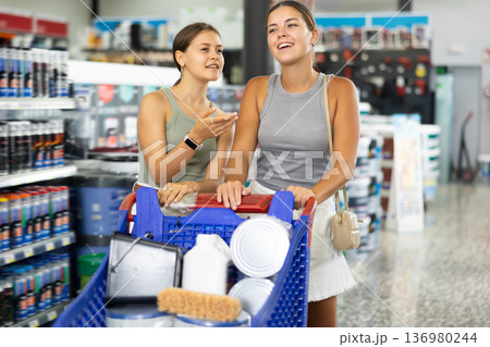 Two smiling female customers with shopping cart chooses paint tools on shelves of hardware store 136980244