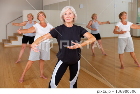 Aged woman practicing ballet dance moves in choreographic studio 136980306