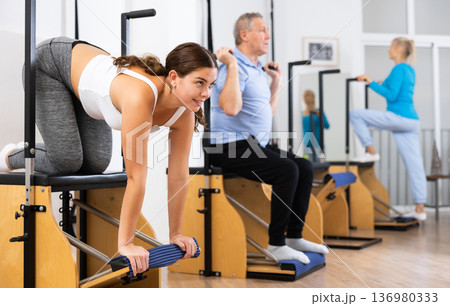 Young European woman making Pilates exercising while standing on knees using Wanda chair machine at gym Young European woman making Pilates exercising while standing on knees using Wanda chair machine at gym 136980333