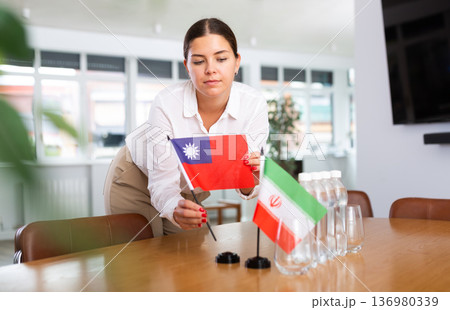 Positive young woman putting little flag of Taiwan on table next to the flag of Iran 136980339