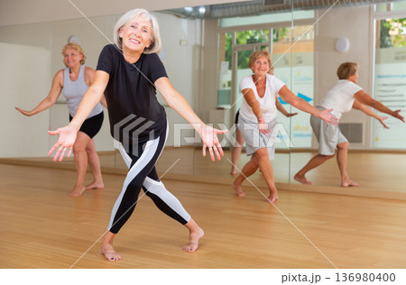 Smiling mature woman enjoying active dancing in dance studio Smiling mature woman enjoying active dancing in dance studio 136980400